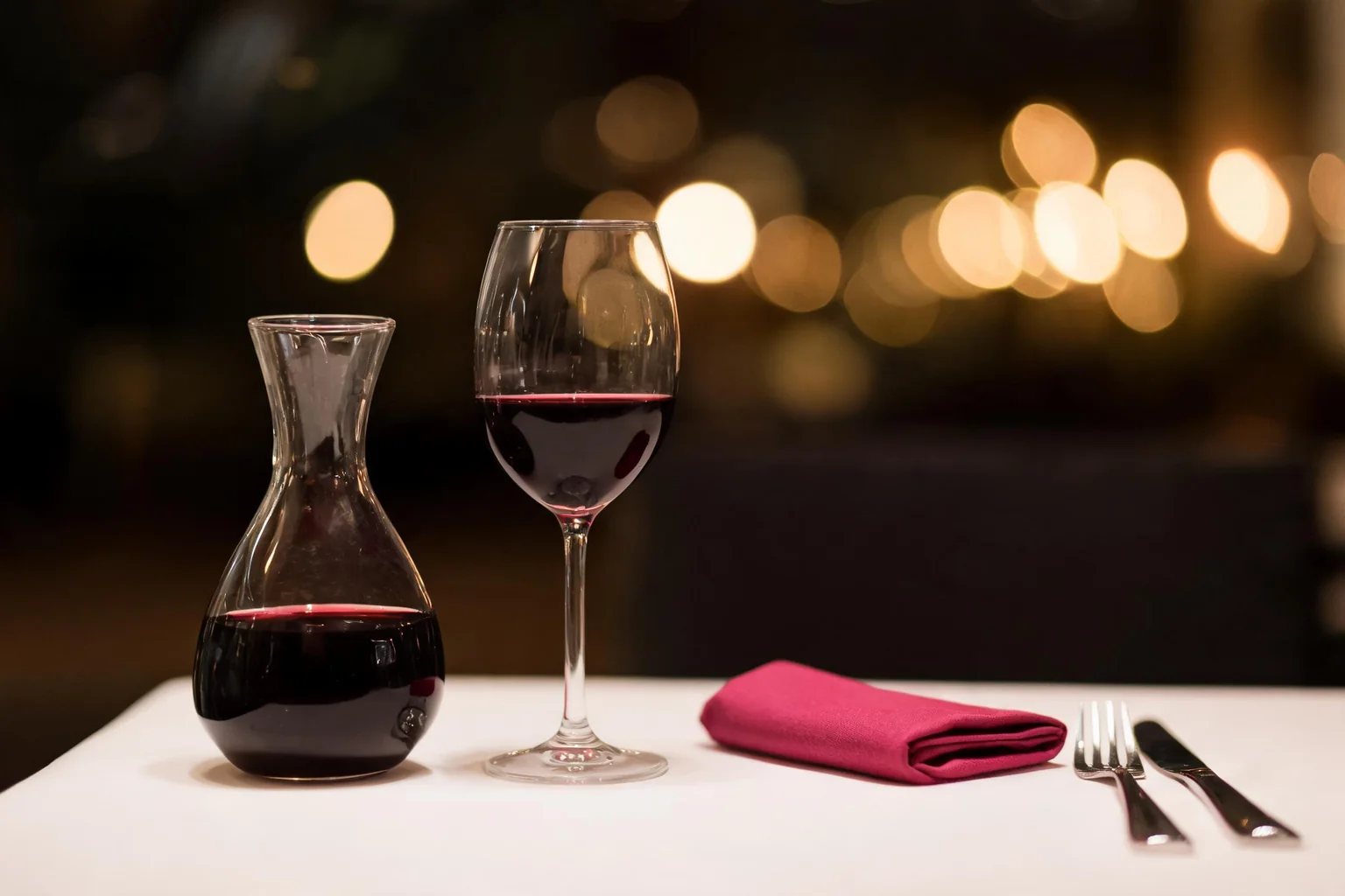 Carafe et verre de vin rouge sur une table blanche, serviette fuchsia